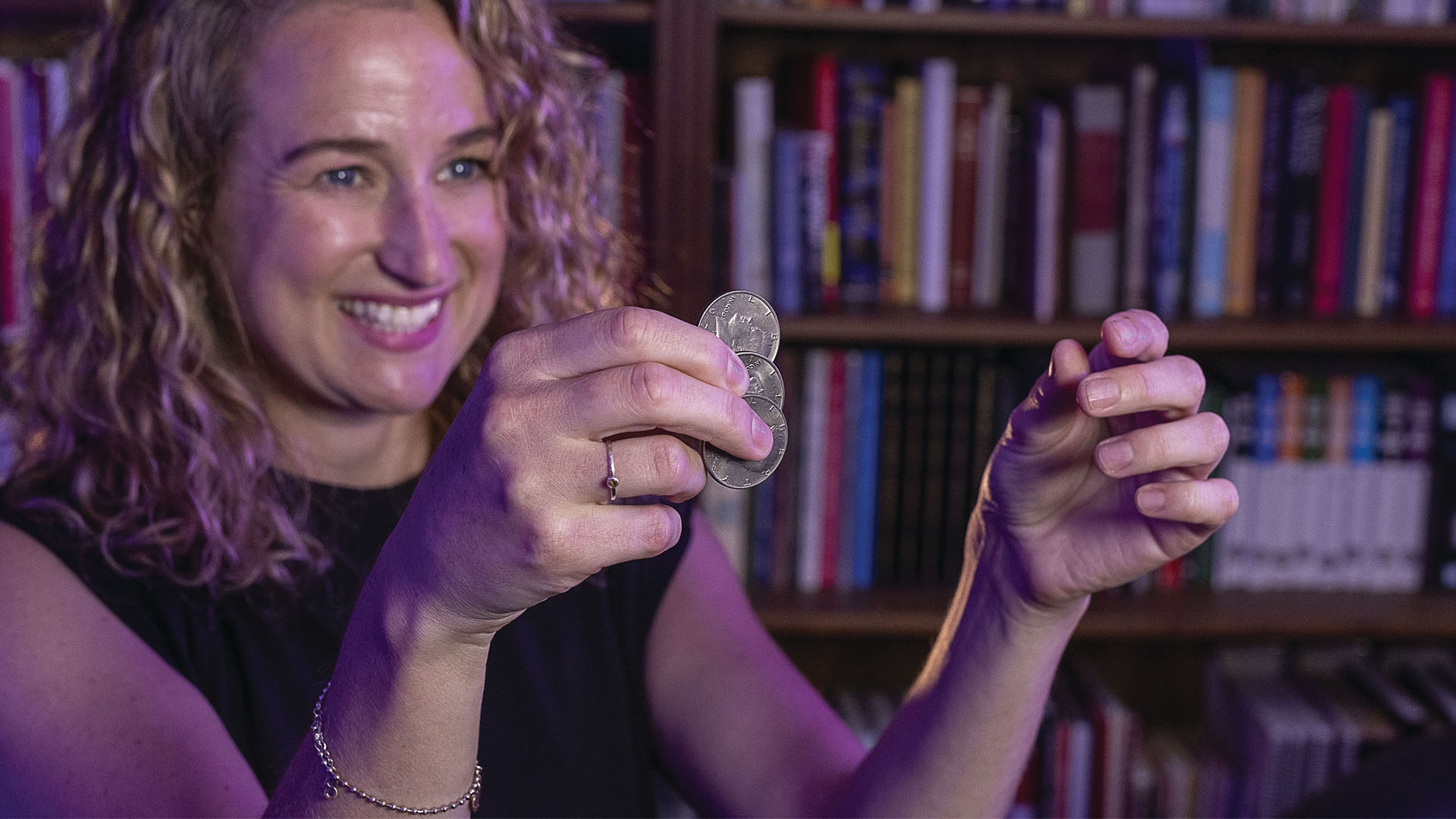 blonde woman performs coin trick with half dollar coins